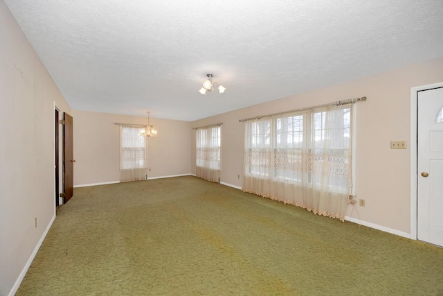 carpeted spare room featuring a textured ceiling, baseboards, and a chandelier