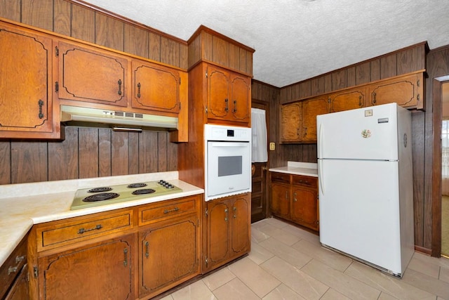 kitchen featuring a textured ceiling, light countertops, white appliances, brown cabinets, and under cabinet range hood