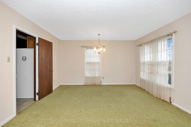 spare room with baseboards, a textured ceiling, a chandelier, and light colored carpet