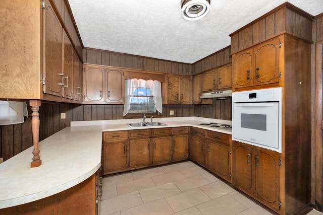 kitchen featuring light countertops, white oven, under cabinet range hood, a sink, and wooden walls