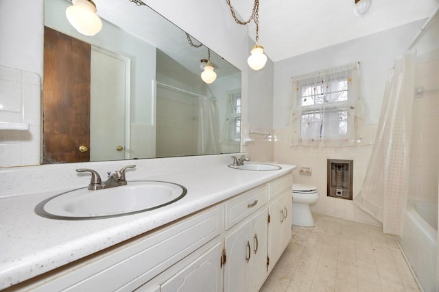 full bath with tile walls, toilet, a sink, heating unit, and double vanity