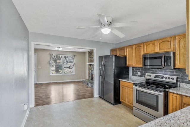 106 Hampton Dr, La Vergne, TN 37086 - kitchen featuring light stone counters, backsplash, a ceiling fan, a fireplace, and appliances with stainless steel finishes