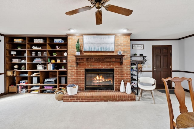 carpeted living room with baseboards, a fireplace, ornamental molding, and a ceiling fan