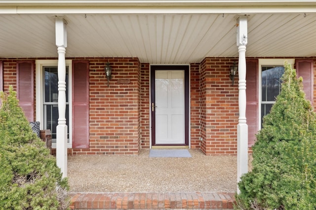 view of exterior entry featuring covered porch and brick siding
