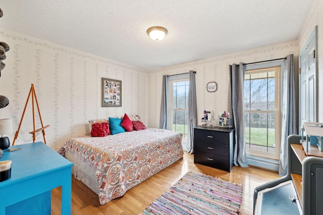 bedroom featuring wallpapered walls, wood finished floors, and a textured ceiling