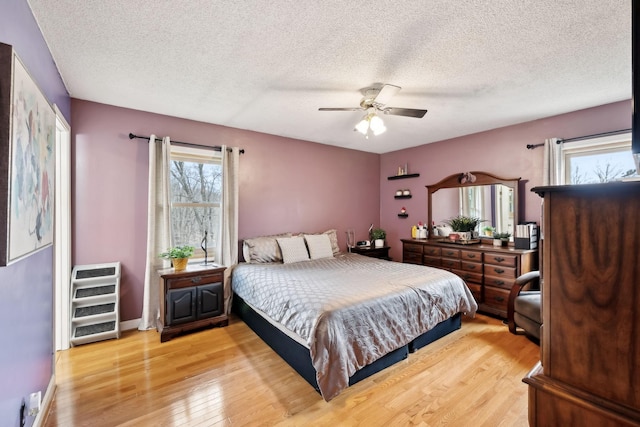 bedroom featuring baseboards, a textured ceiling, light wood-style floors, and a ceiling fan