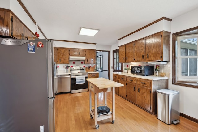 kitchen featuring decorative backsplash, light countertops, stainless steel appliances, under cabinet range hood, and light wood-style floors
