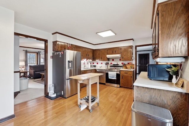 kitchen with light countertops, a sink, under cabinet range hood, stainless steel appliances, and light wood-style floors