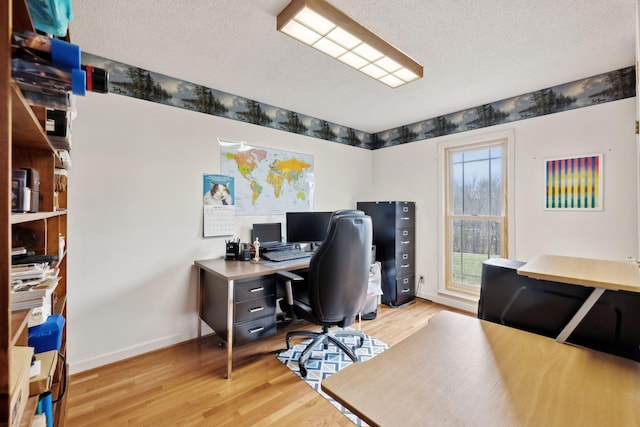 office area featuring baseboards, light wood-type flooring, and a textured ceiling