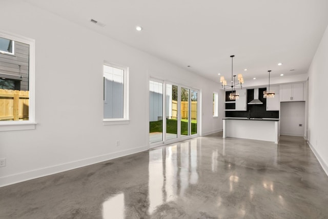 unfurnished living room featuring finished concrete floors, baseboards, visible vents, recessed lighting, and an inviting chandelier