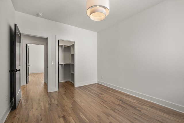 unfurnished bedroom featuring a spacious closet, a closet, baseboards, and wood finished floors