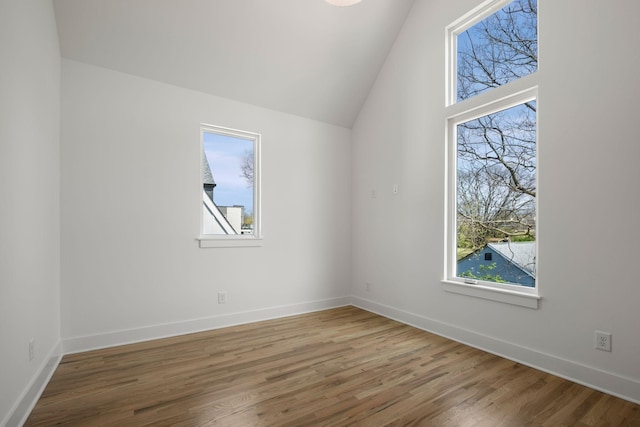 spare room featuring baseboards, vaulted ceiling, wood finished floors, and a healthy amount of sunlight
