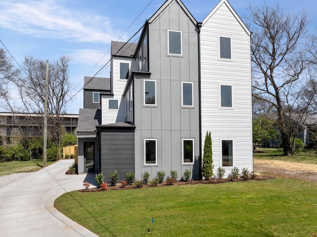view of side of property with a lawn, board and batten siding, concrete driveway, and roof with shingles
