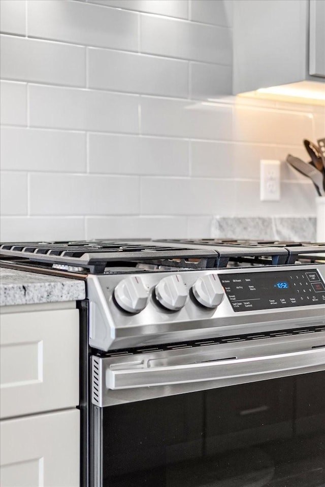 interior details with light stone countertops, backsplash, and stainless steel gas stove