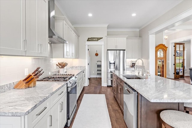 kitchen featuring appliances with stainless steel finishes, wall chimney exhaust hood, decorative backsplash, and a sink