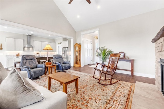 living room featuring baseboards, high vaulted ceiling, a ceiling fan, and a stone fireplace