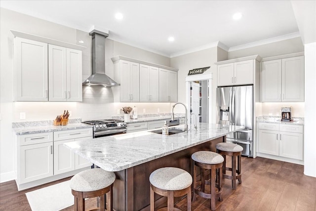 kitchen featuring stainless steel appliances, wall chimney range hood, dark wood-style flooring, a kitchen bar, and a sink