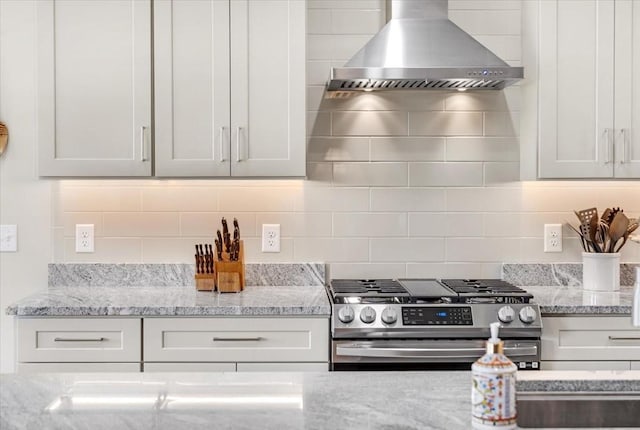 kitchen featuring white cabinets, gas range, wall chimney range hood, and light stone counters