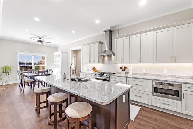 kitchen featuring a sink, stainless steel appliances, a kitchen bar, wall chimney exhaust hood, and a ceiling fan