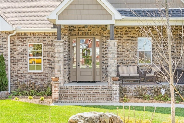 view of exterior entry with a shingled roof and brick siding