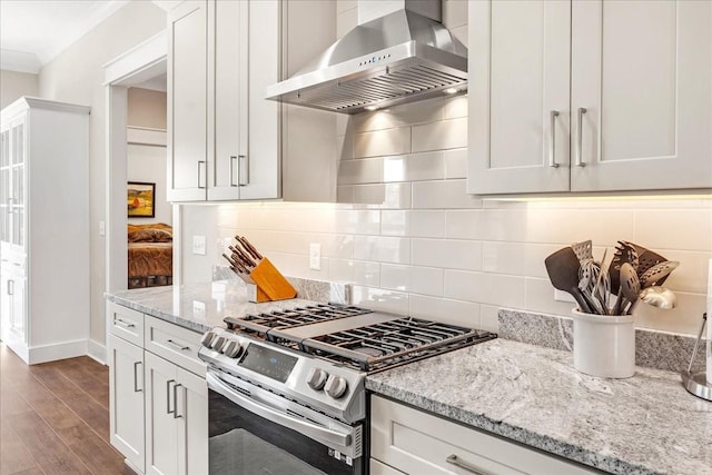 kitchen featuring stainless steel gas range oven, light stone countertops, wall chimney exhaust hood, wood finished floors, and backsplash