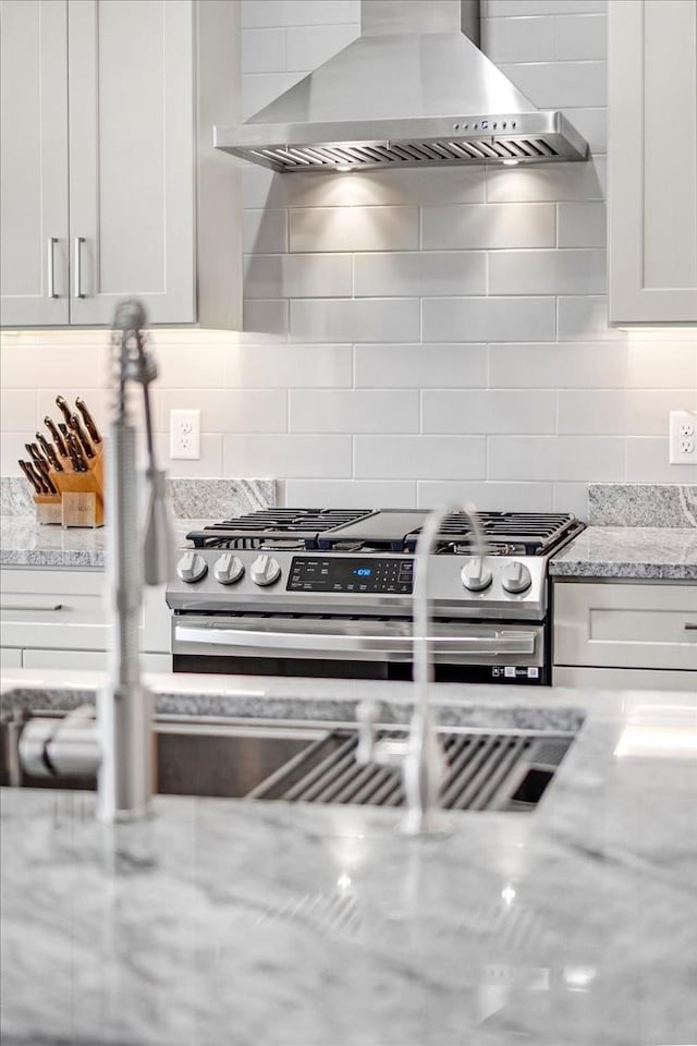 kitchen with light stone counters, decorative backsplash, white cabinets, and wall chimney exhaust hood