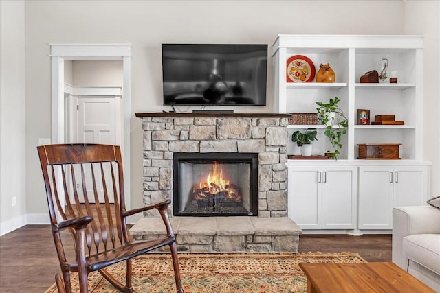 interior space with dark wood-type flooring, a stone fireplace, and baseboards