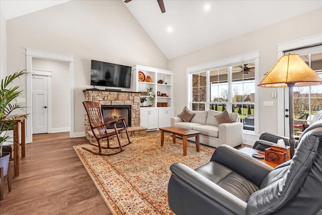 living area featuring wood finished floors, a fireplace, baseboards, high vaulted ceiling, and a ceiling fan