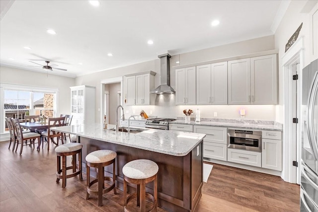 kitchen featuring wall chimney range hood, a sink, a breakfast bar, ceiling fan, and stainless steel appliances