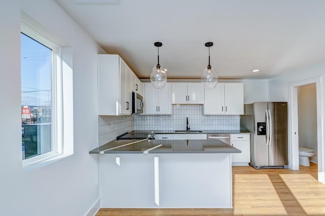 kitchen featuring dark countertops, appliances with stainless steel finishes, a sink, light wood finished floors, and a peninsula
