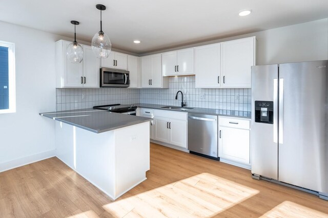 kitchen with a peninsula, light wood-style floors, white cabinetry, a sink, and appliances with stainless steel finishes