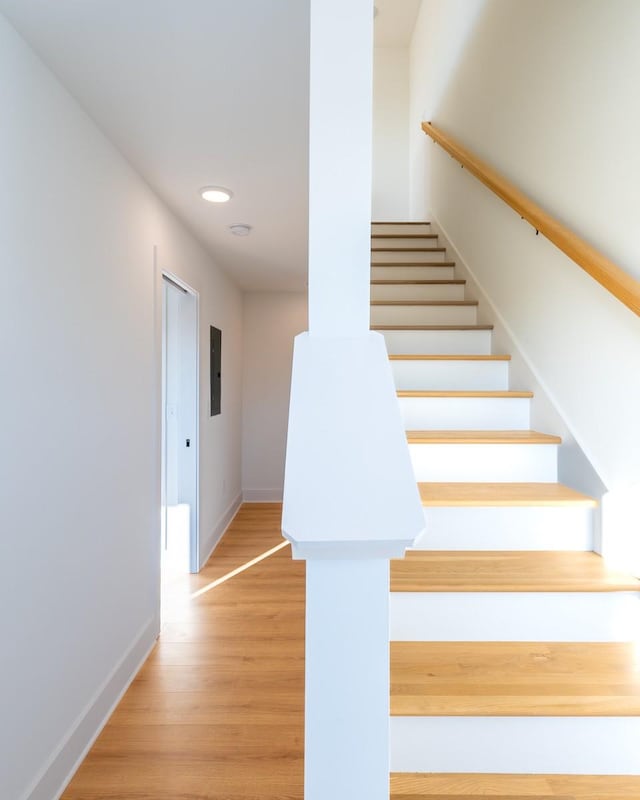 stairway with baseboards, electric panel, and wood finished floors