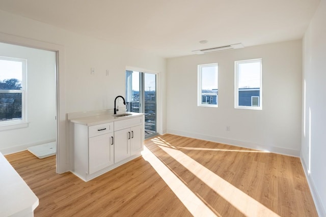 kitchen featuring baseboards, light countertops, white cabinets, a sink, and light wood finished floors