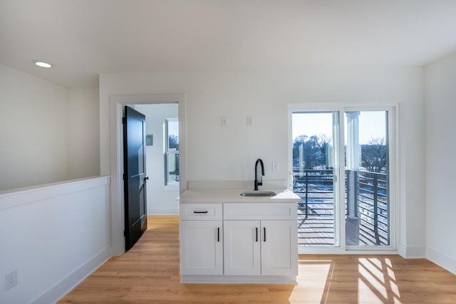 kitchen featuring a sink, baseboards, light countertops, light wood-style floors, and white cabinetry