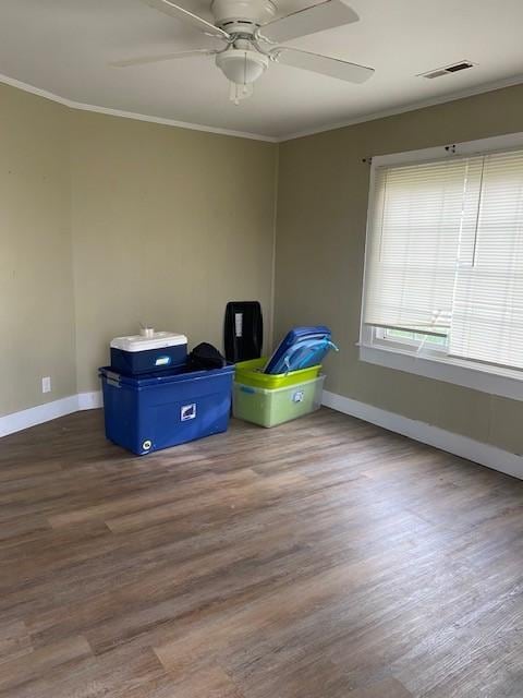 unfurnished room featuring crown molding, dark wood-type flooring, baseboards, ceiling fan, and visible vents