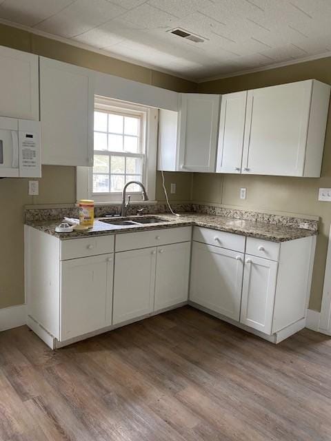 kitchen featuring a sink, light wood-style floors, visible vents, white cabinets, and white microwave