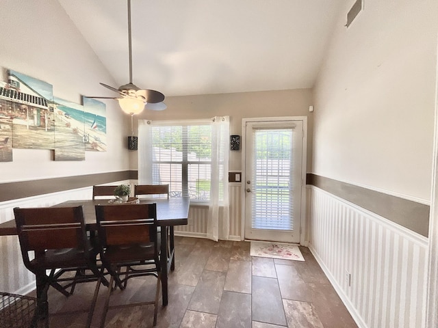 dining space with a ceiling fan, vaulted ceiling, wainscoting, and visible vents