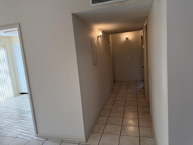 corridor featuring electric panel, light tile patterned floors, and a textured ceiling