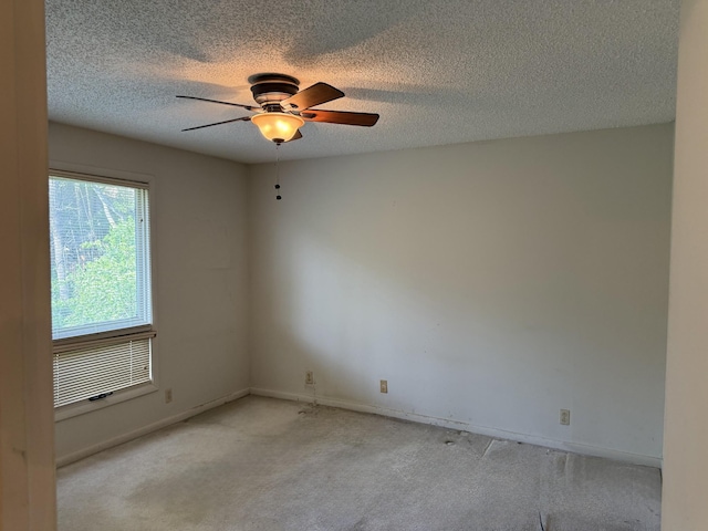 empty room featuring light carpet, baseboards, a ceiling fan, and a textured ceiling