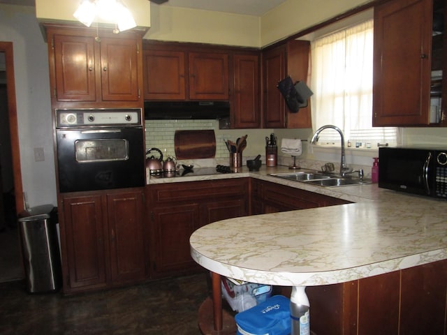 kitchen featuring light countertops, a sink, a peninsula, under cabinet range hood, and black appliances