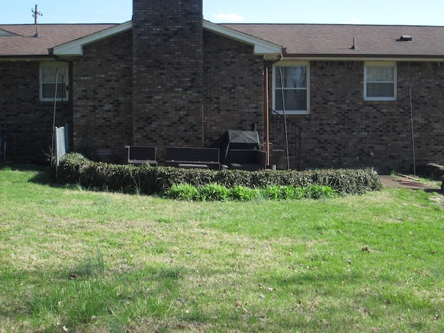 exterior space featuring brick siding, a yard, and a chimney