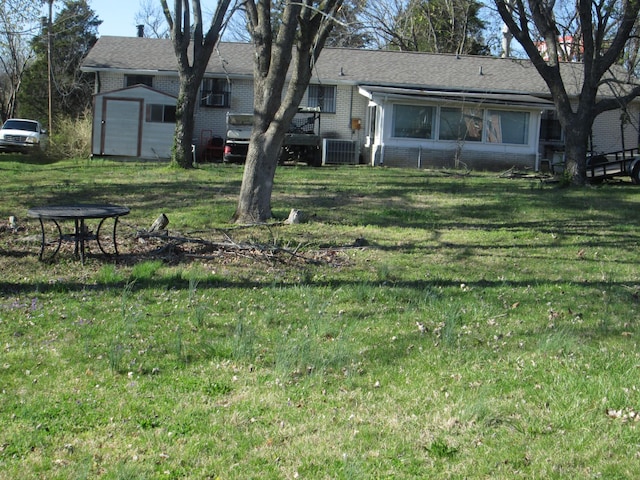 back of property featuring central air condition unit, a storage shed, brick siding, an outdoor structure, and a yard