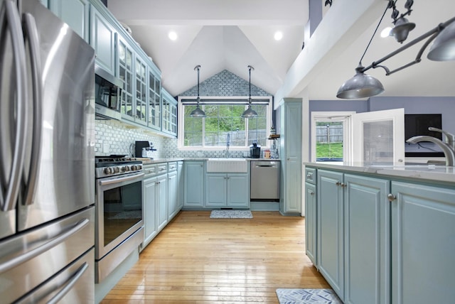 kitchen featuring vaulted ceiling, stainless steel appliances, backsplash, a sink, and light wood finished floors