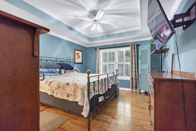 bedroom featuring a ceiling fan, a raised ceiling, wood finished floors, baseboards, and ornamental molding