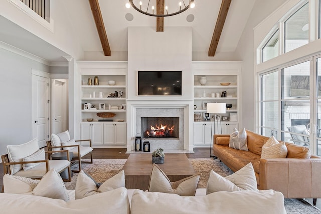 living area featuring an inviting chandelier, a towering ceiling, beam ceiling, a fireplace, and wood finished floors
