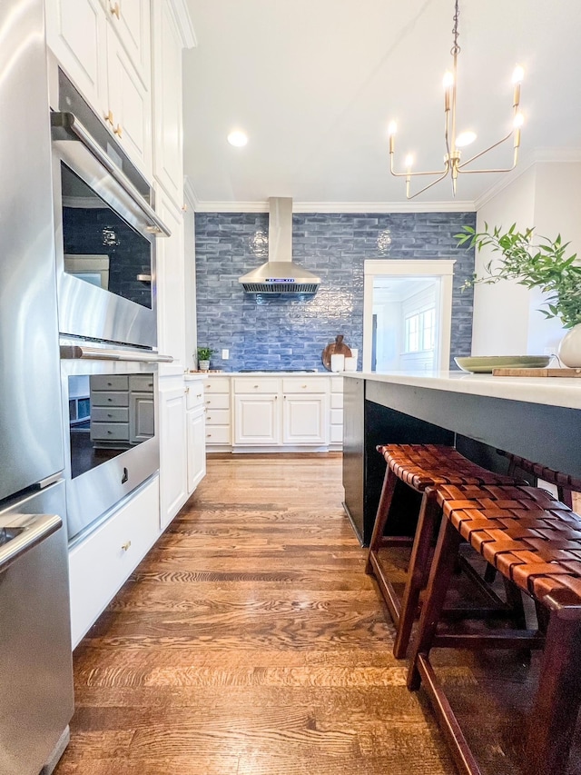336 Chesterfield Ave, Nashville, TN 37212 - kitchen with white cabinets, ornamental molding, wall chimney range hood, light wood-style flooring, and appliances with stainless steel finishes