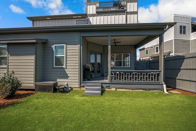 rear view of property with a lawn, fence, board and batten siding, and a ceiling fan