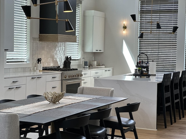 kitchen with high end range, tasteful backsplash, light wood-style floors, and white cabinetry