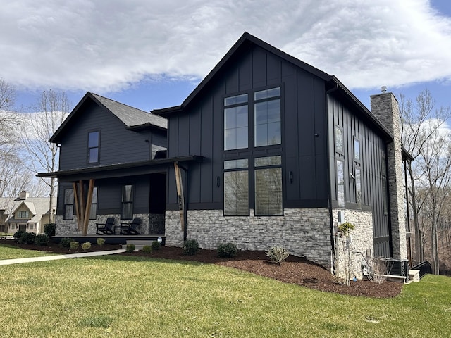 view of front of house with board and batten siding, a front lawn, a chimney, and covered porch