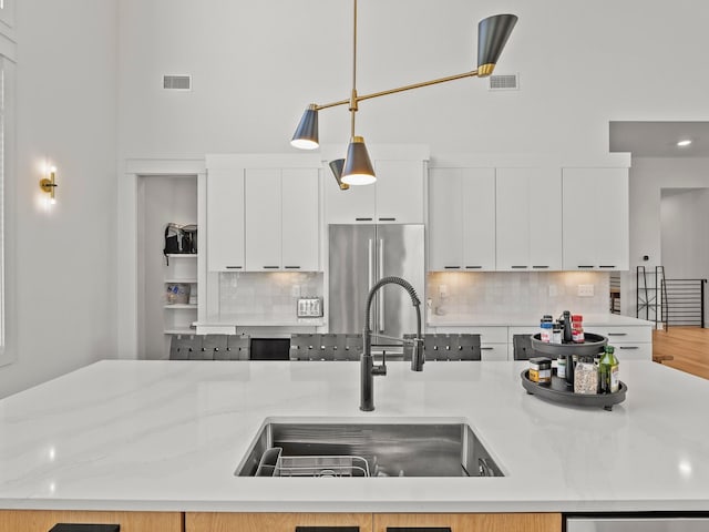 kitchen with decorative backsplash, a sink, visible vents, and freestanding refrigerator